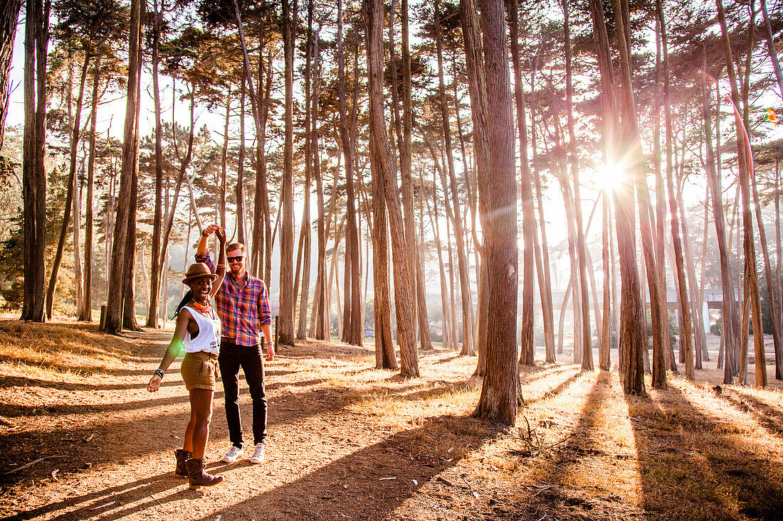 Couple holding hands under trees in sunny forest, San Francisco, California, United States