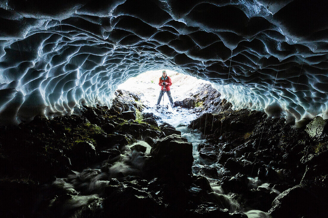 Caucasian hiker viewing stream from entrance of ice cave, Iceland, Iceland, Iceland