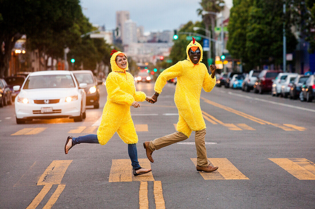 Couple in chicken costumes crossing city street, San Francisco, California, United States