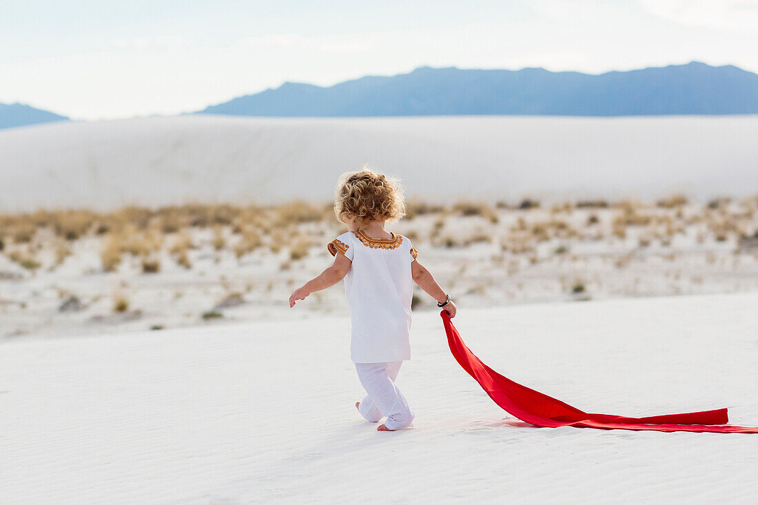Caucasian boy playing with scarf on sand dune, White Sands, New Mexico, USA