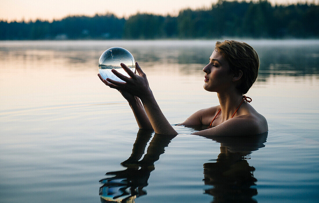 Caucasian woman holding crystal ball in still lake, Bremerton, Wa, USA