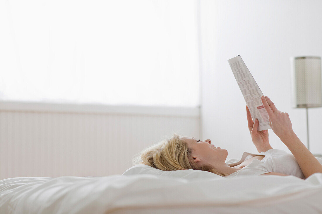 Caucasian woman laying in bed reading paperwork, Saint Louis, MO, USA