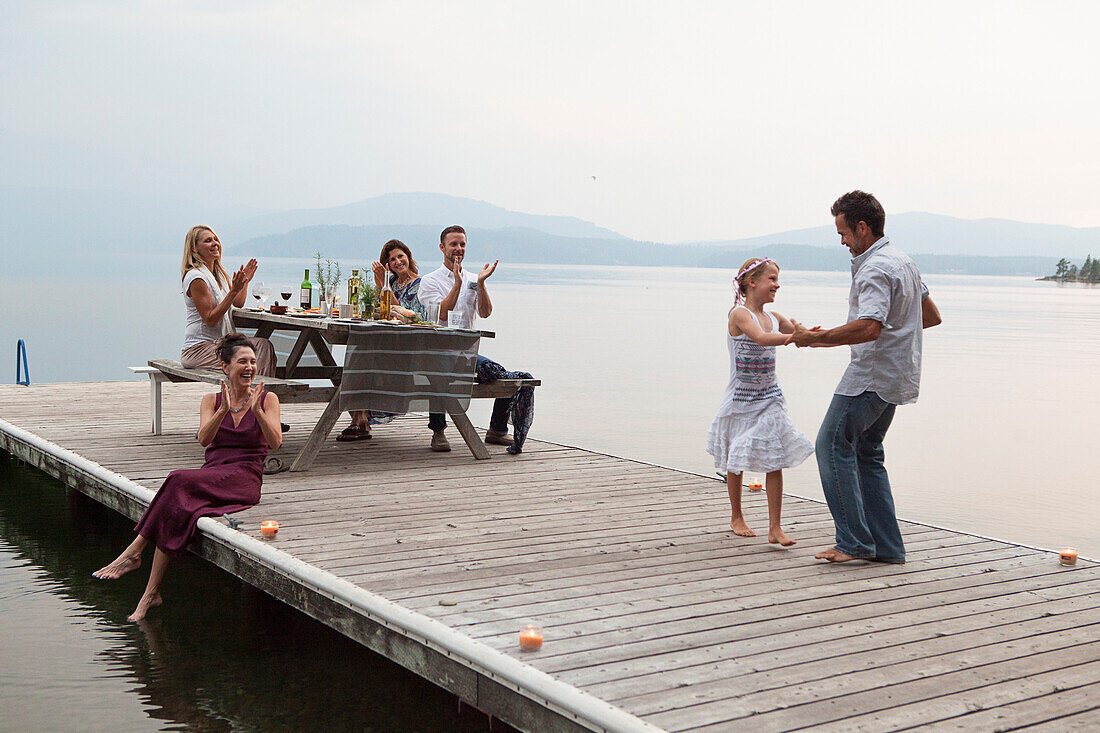 Caucasian family cheering as father and daughter dance on pier over lake, Hope, Idaho, USA