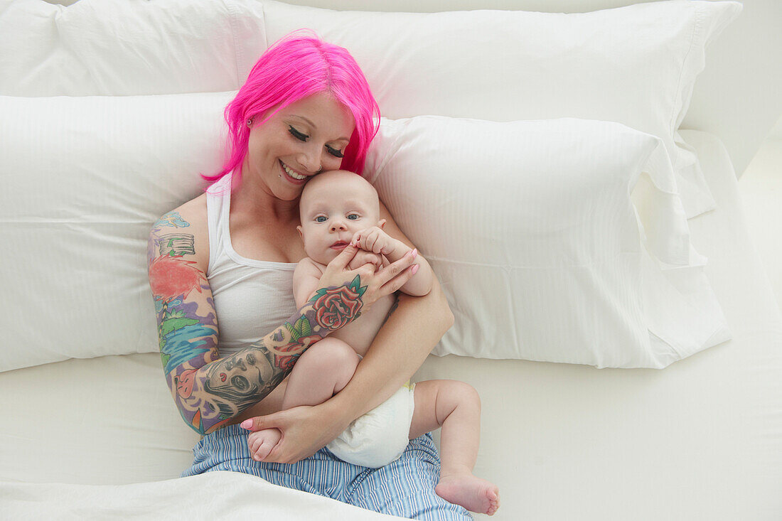 Caucasian mother with pink hair and tattoos cradling baby, Toronto, Ontario, Canada