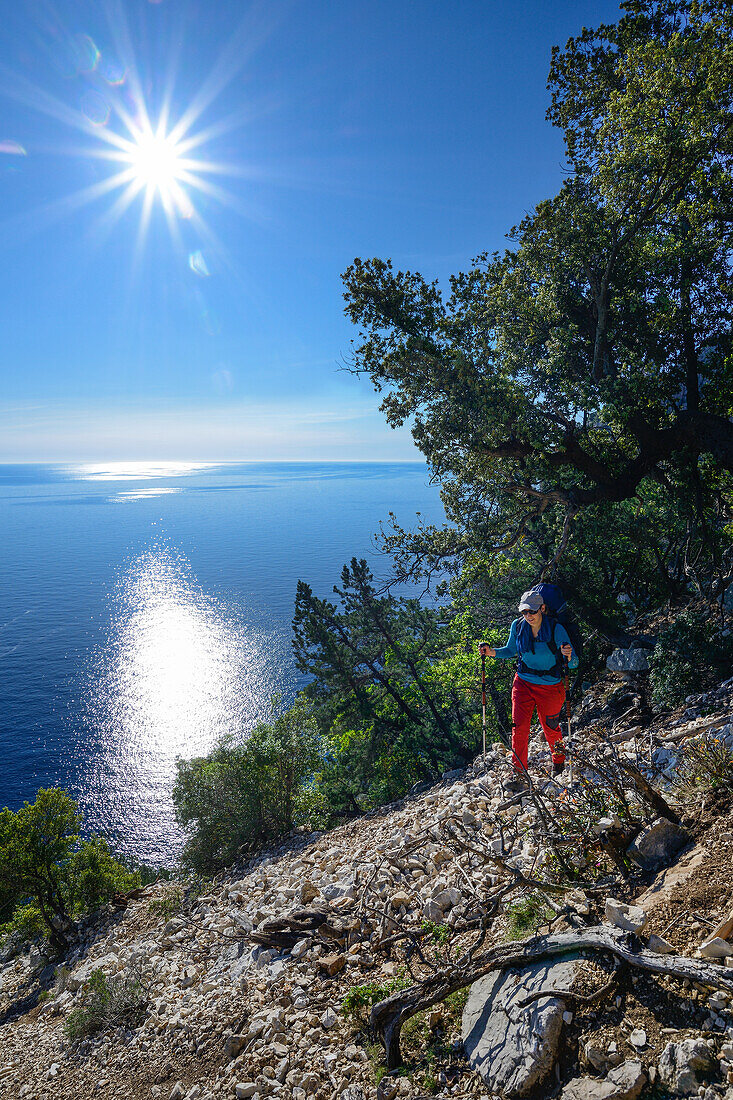 Eine junge Frau mit Trekkingausrüstung wandert oberhalb des Meeres entlang der gebirgigen Küste, Golfo di Orosei, Selvaggio Blu, Sardinien, Italien, Europa