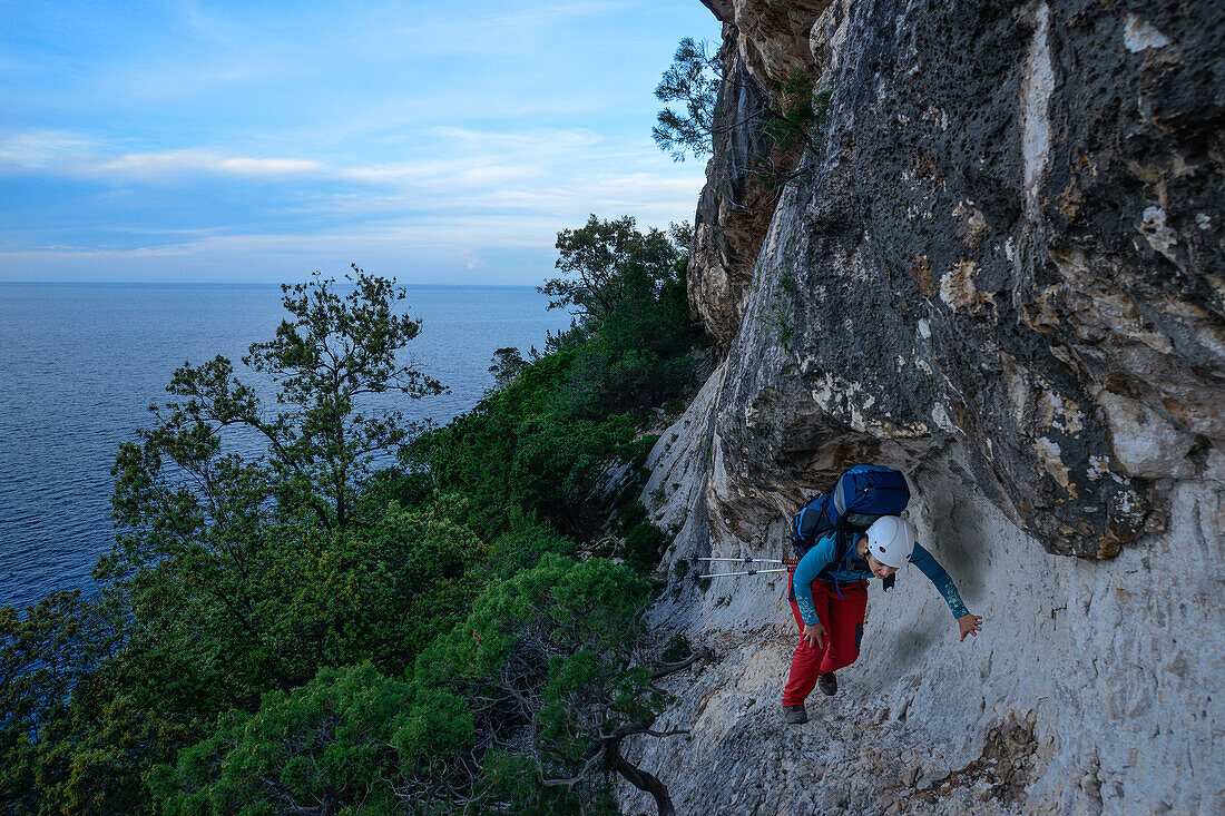 Eine junge Frau mit Trekkingausrüstung läuft auf ausgesetztem Band oberhalb des Meeres entlang der gebirgigen Küste, Golfo di Orosei, Selvaggio Blu, Sardinien, Italien, Europa