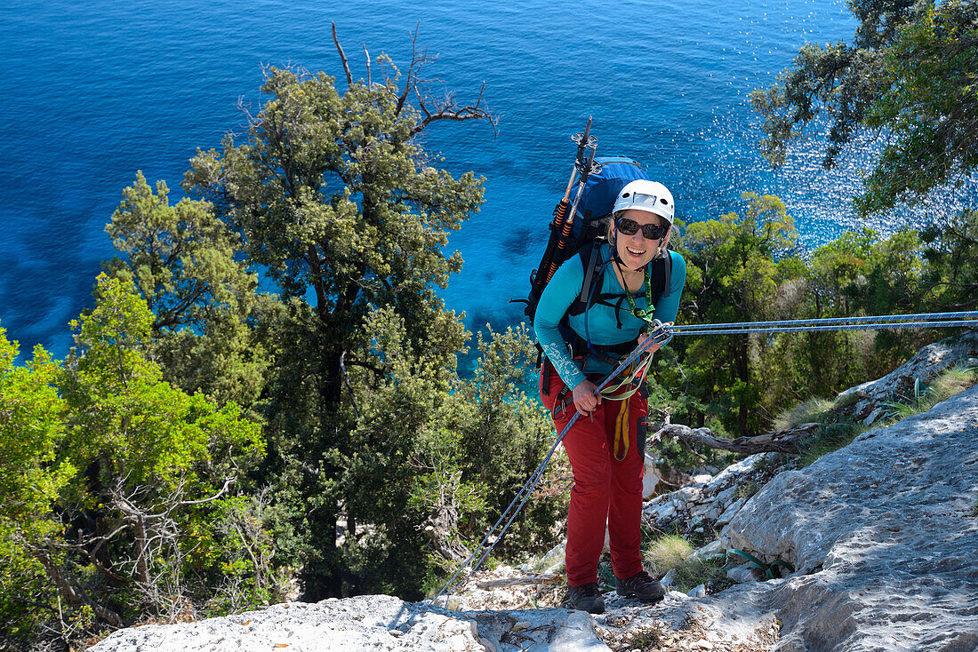 Eine junge Frau mit Trekkingausrüstung seilt sich oberhalb des Meeres in der gebirgigen Küstenlandschaft ab, Golfo di Orosei, Selvaggio Blu, Sardinien, Italien, Europa