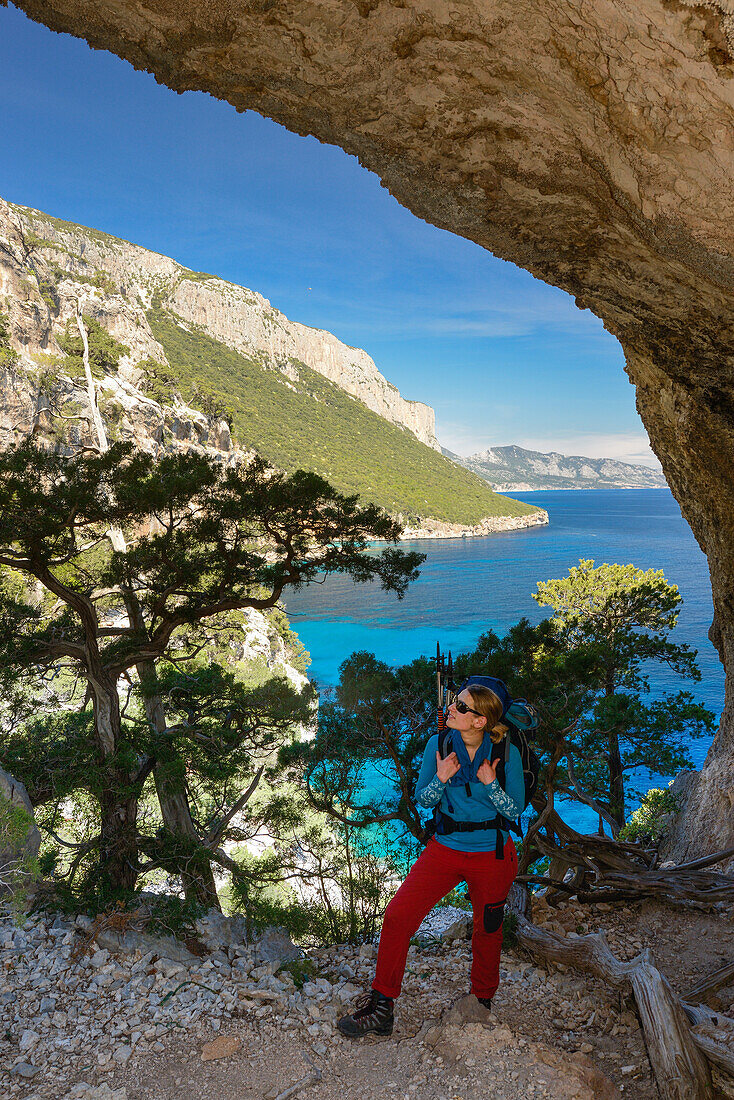 A young woman with trekking gear hikes through the rock arch Arcu su Feilau at the mountainous coast above the sea, Golfo di Orosei, Selvaggio Blu, Sardinia, Italy, Europe