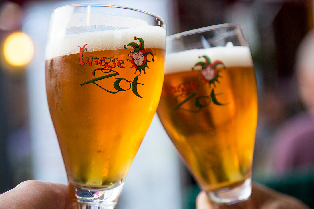 Anstossen mit zwei Gläsern Brugse Zot Bier in einem Restaurant in der Altstadt, Brügge, Flandern, Belgien, Europa