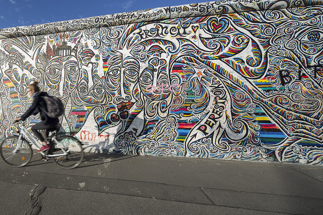 Woman riding her bicycle past the Berlin Wall, East Side Gallery, Friedrichshain, Berlin, Germany