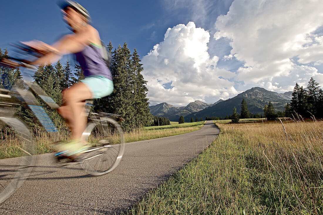 Junge Frau fährt mit ihrem Fahrrad in der Nähe der Berge an einem sonnigen Tag, Tannheimer Tal, Tirol, Österreich