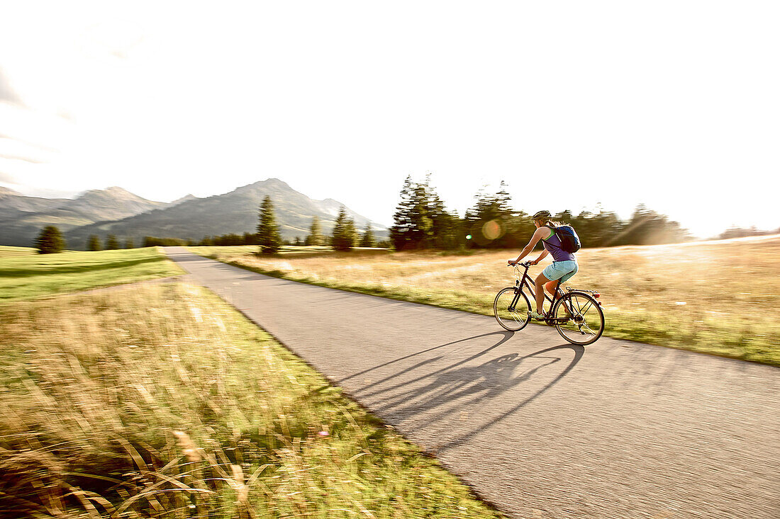 Junge Frau fährt Fahrrad an einem sonnigen Tag, Tannheimer Tal, Tirol, Österreich