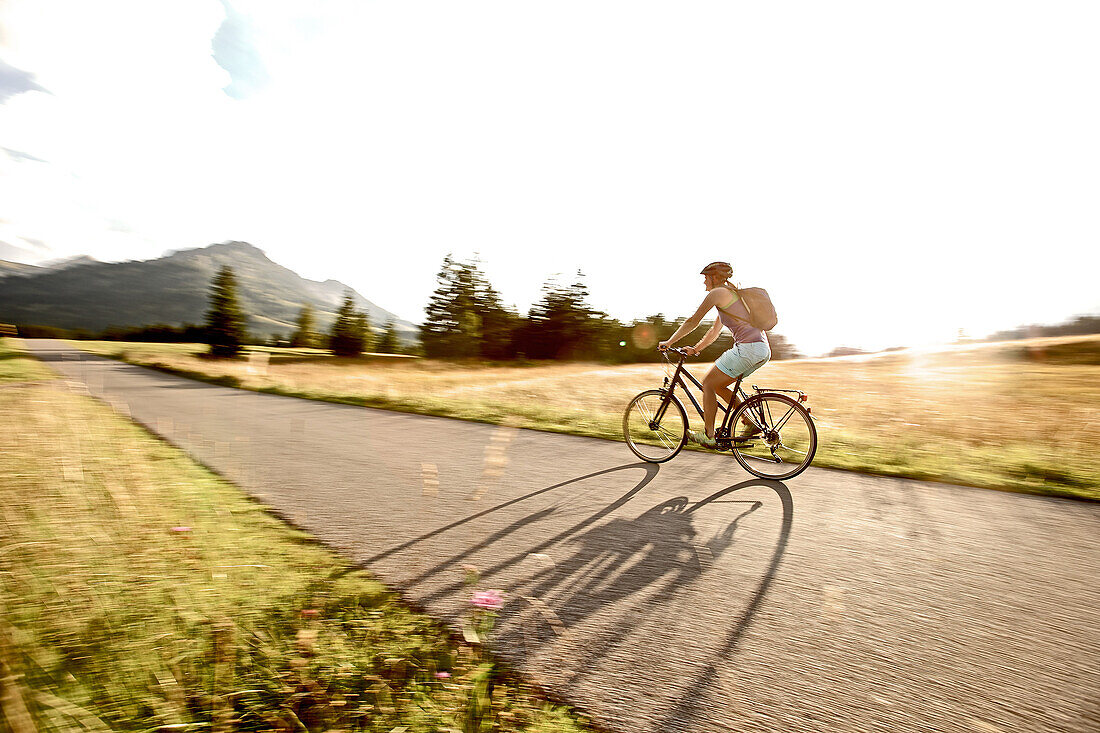 Young woman riding her bike near a meadow on a sunny day, Tannheimer Tal, Tyrol, Austria