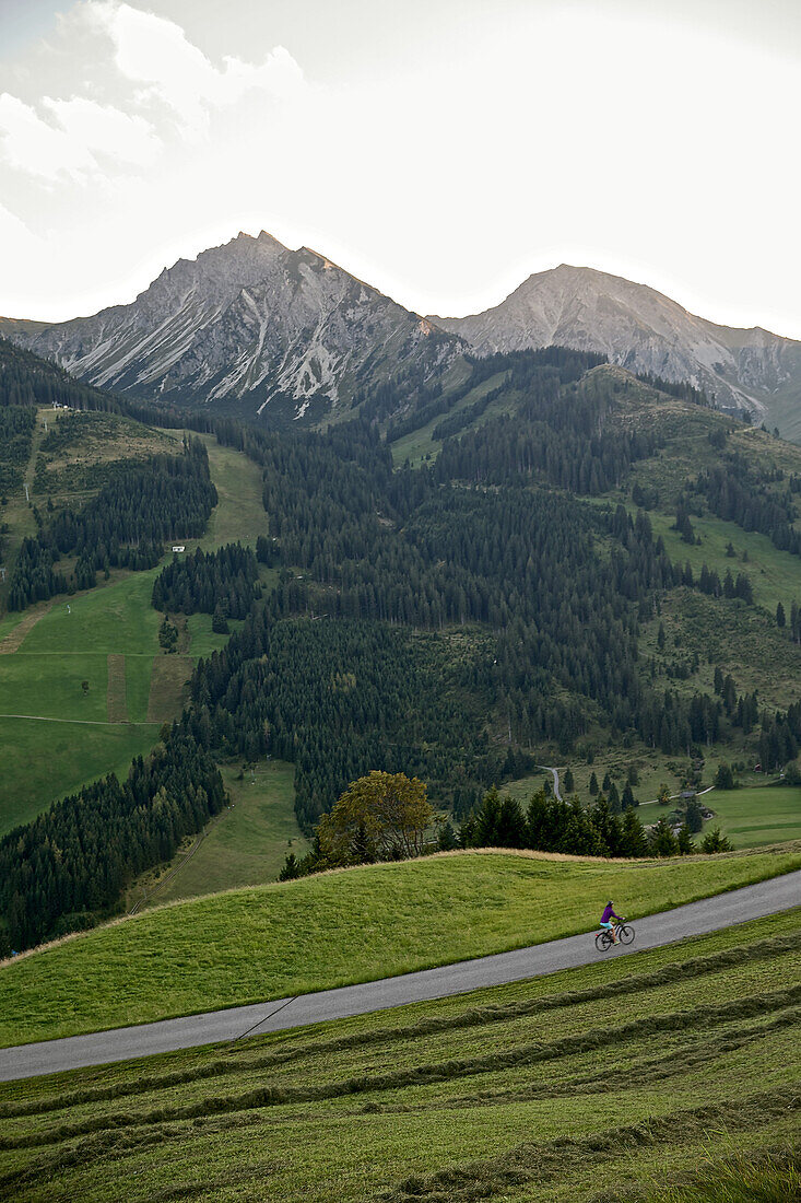 Young woman riding her bike near mountains on a sunny day, Tannheimer Tal, Tyrol, Austria