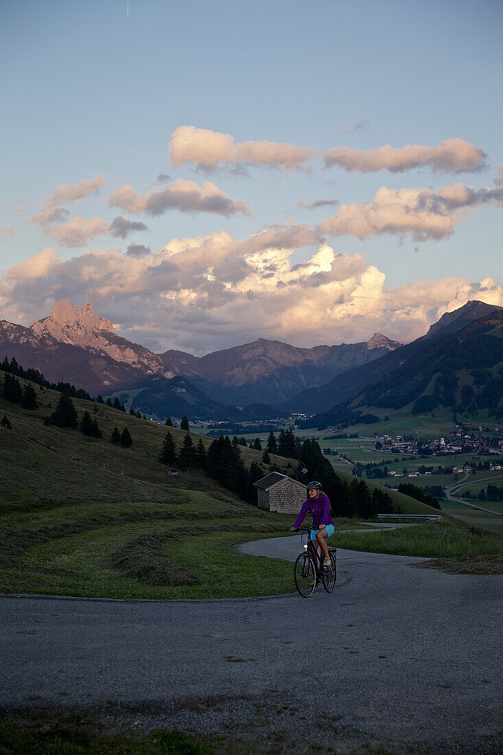 Junge Frau fährt mit ihrem Fahrad in der Nähe der Berge bei Sonnenuntergang, Rote Flüh, Gimpel, Hochwiesler, Tannheimer Tal, Tirol, Österreich