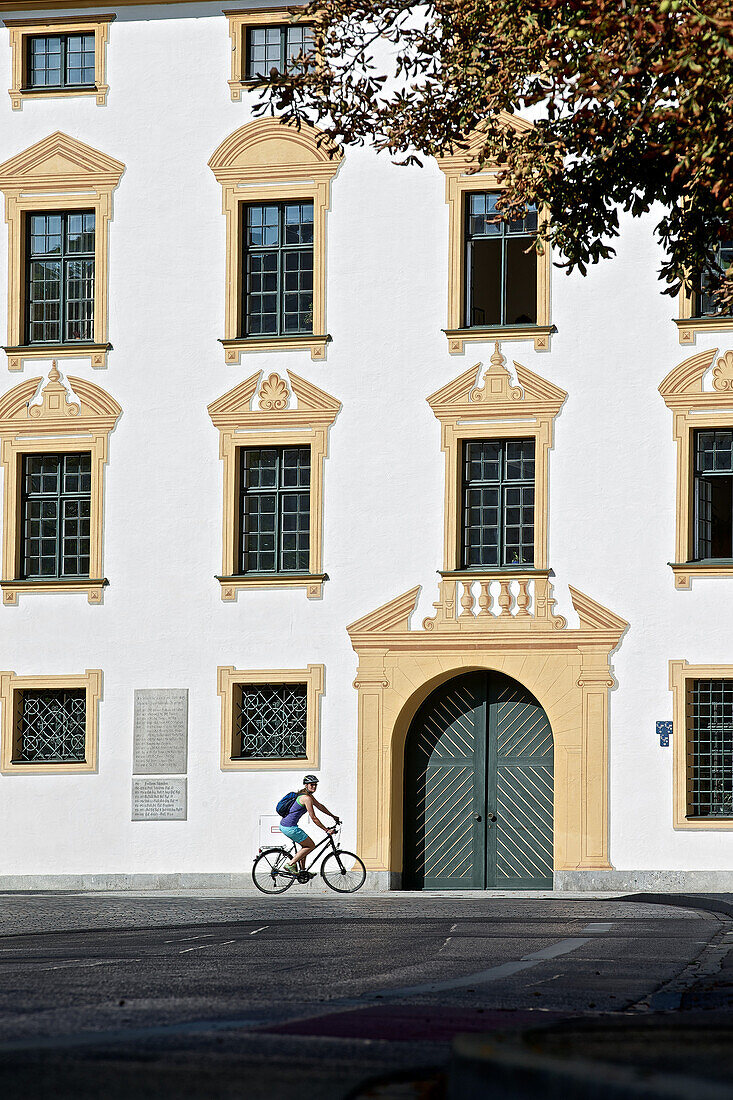 Junge Fahrradfahrerin fährt vor einem großen Gebäude, Kempten, Bayern, Deutschland