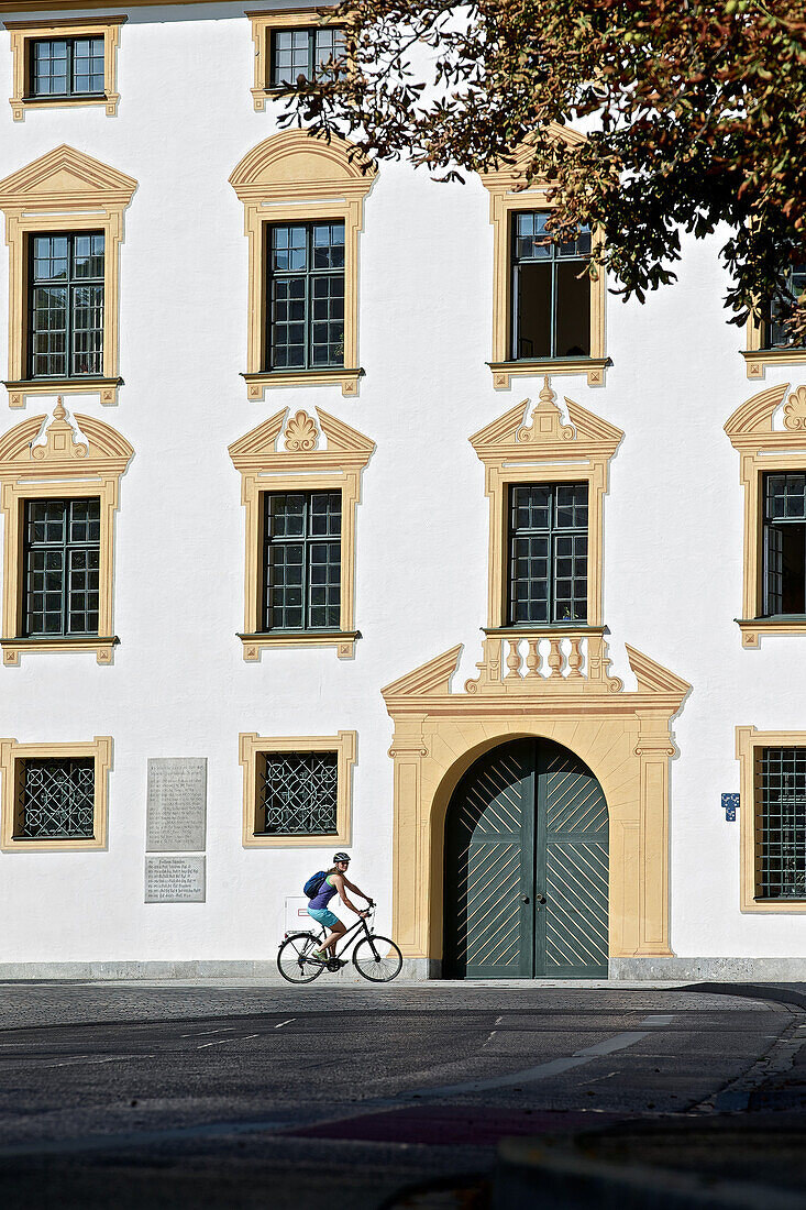 Young female cyclist riding her bike in front of a large building, Kempten, Bavaria, Germany