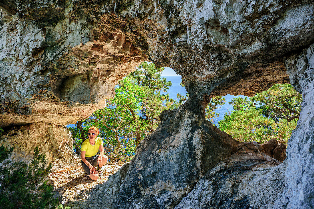 Frau sitzt an Felsbogen, Selvaggio Blu, Nationalpark Golfo di Orosei e del Gennargentu, Sardinien, Italien