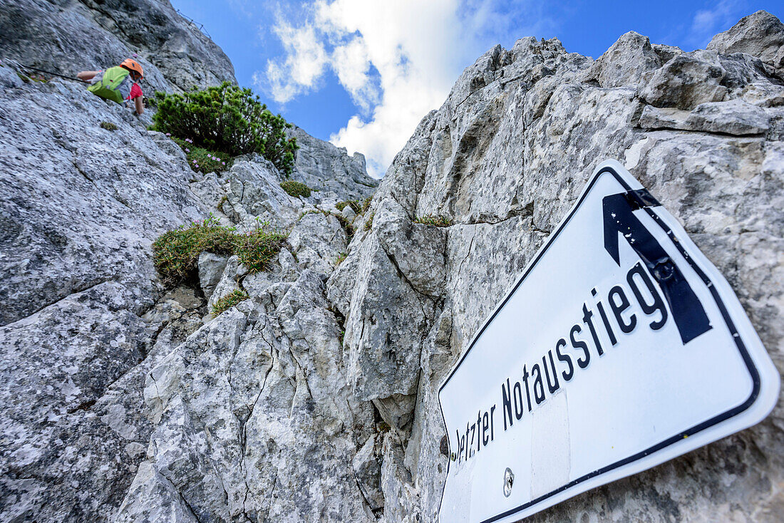 Schild Notausstieg am Pidinger Klettersteig mit Frau im Hintergrund, Pidinger Klettersteig, Hochstaufen, Chiemgauer Alpen, Chiemgau, Oberbayern, Bayern, Deutschland
