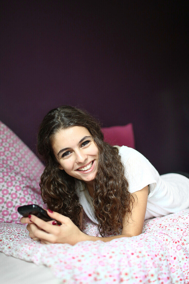 A teenage girl with her cell phone on her bed