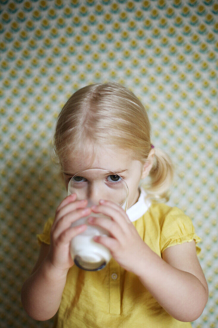 A 2 years old girl posing as she 's drinking a glass of milk