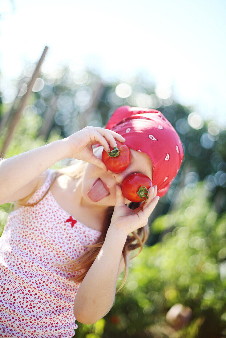 Girl holding up tomatoes up to her eyes and sticking out one's tongue