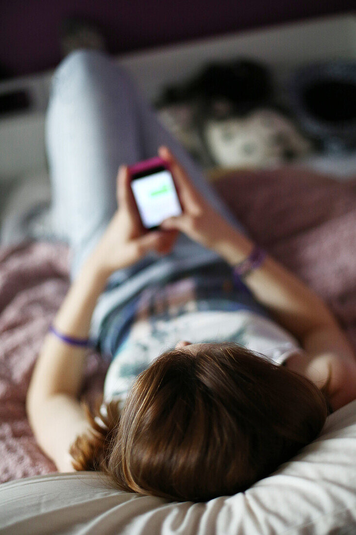 A teenager (girl) on her bed using her mobile, back view