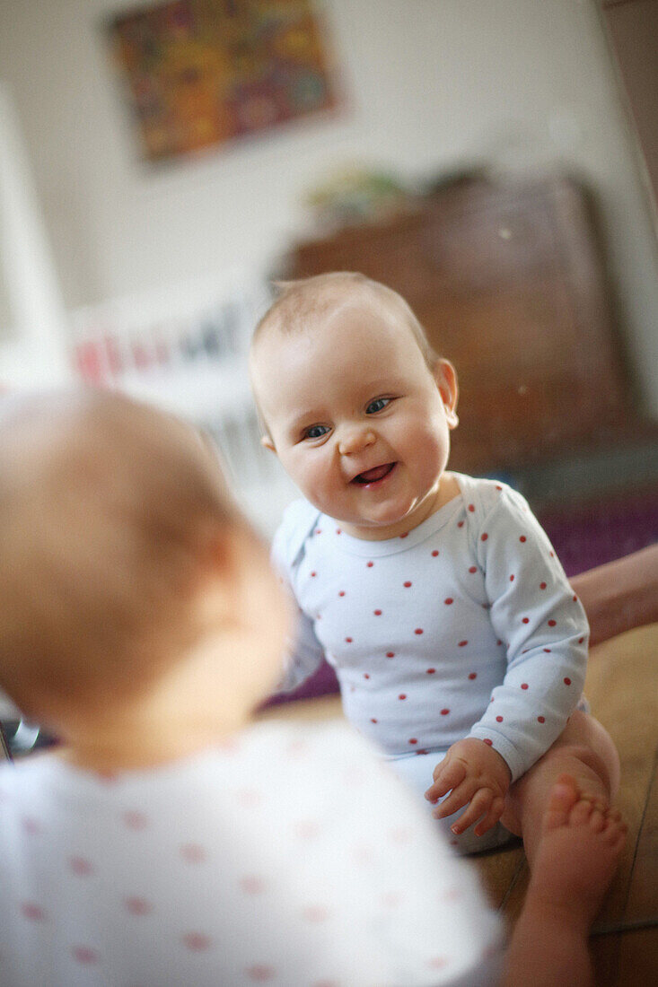 A 10 months baby girl smiling in front of a mirror