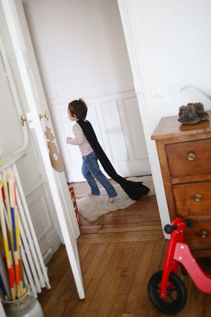 Little boy playing with a black cape, he runs in a hallway