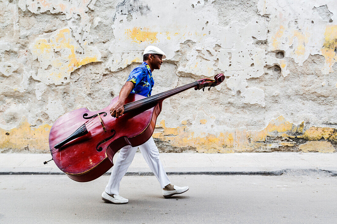 Hispanic musician carrying bass on city street