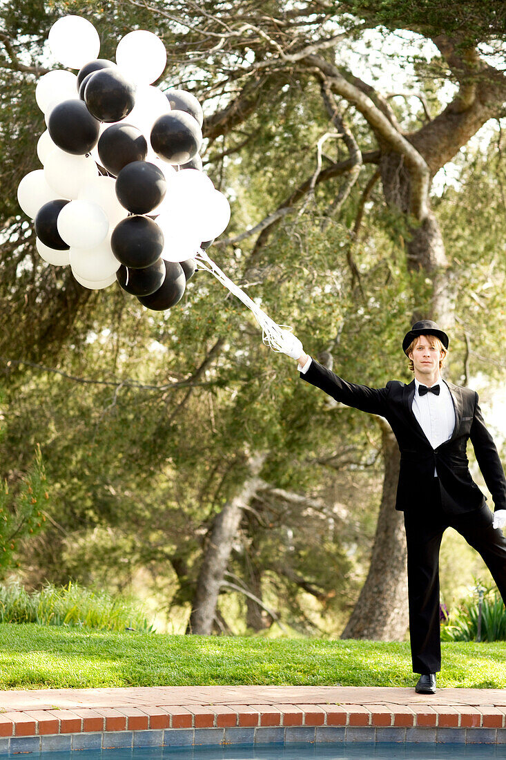 Caucasian man in tuxedo holding bunch of balloons