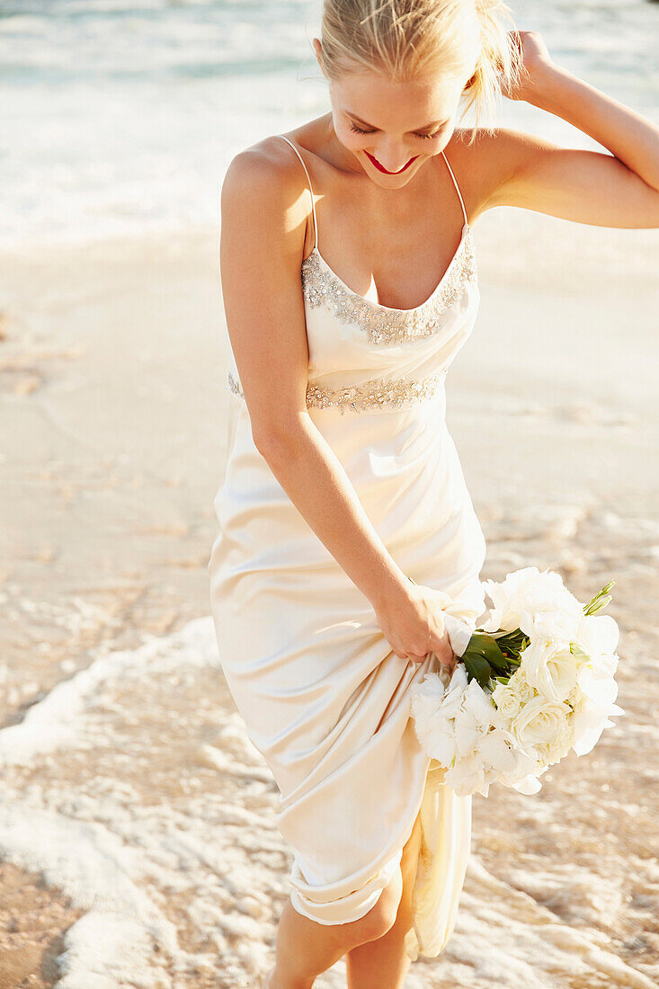 Caucasian bride holding bouquet on beach