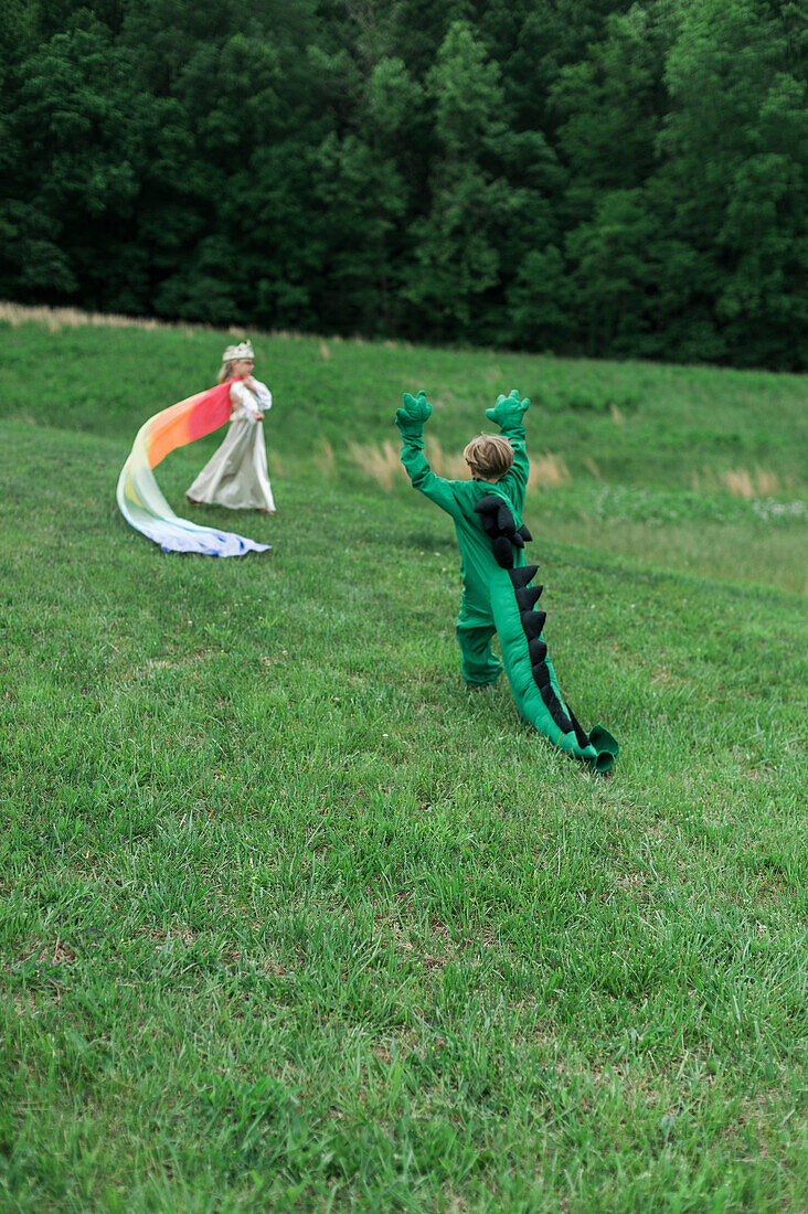 Young Boy in Dragon Costume Playing with Young Girl in Princess Costume in Grassy Field