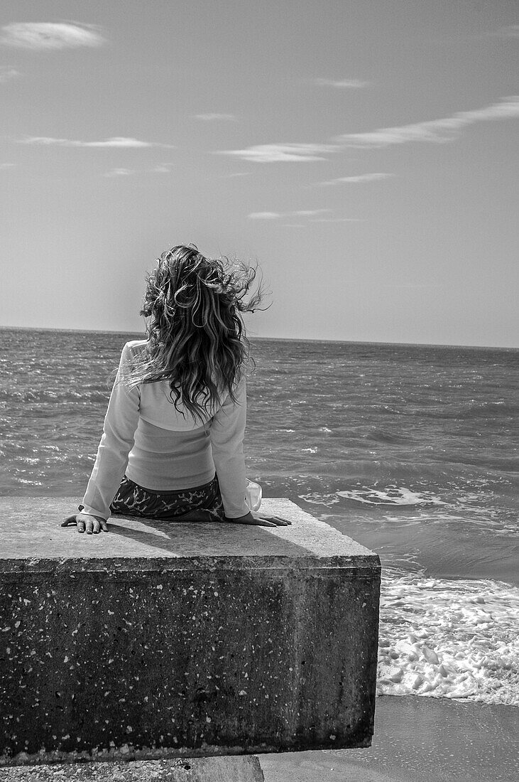 Young Girl Sitting on Stone Slab Looking out to Sea, Rear View