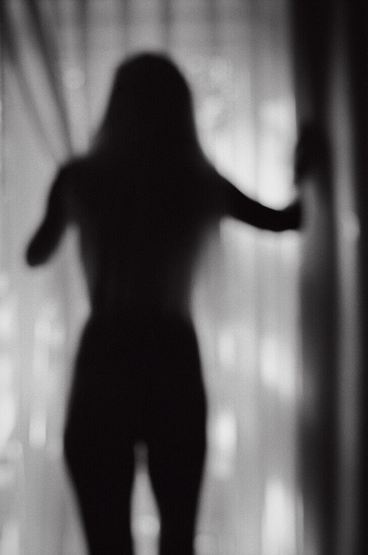 Silhouette einer nackten Frau, die am Fenster steht, Rückansicht