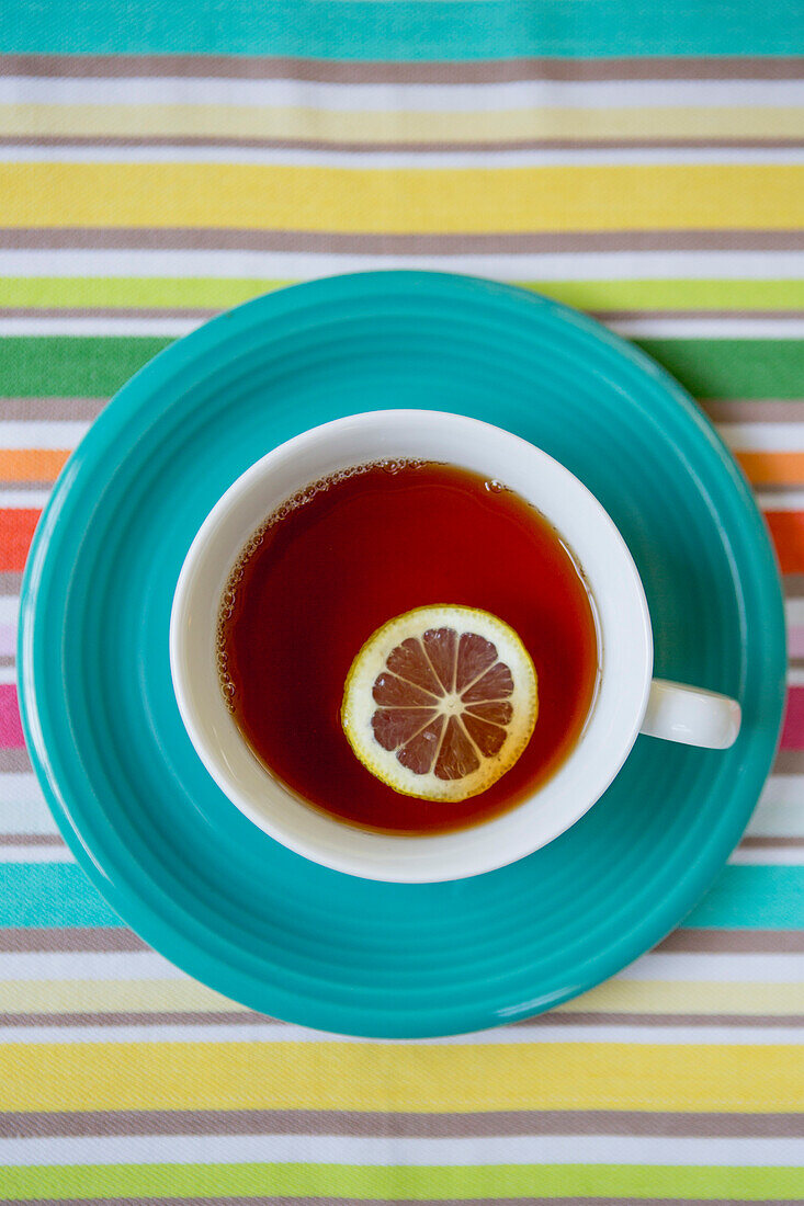 Cup of Tea With Slice of Lemon on Blue Plate and Striped Tablecloth, High Angle View