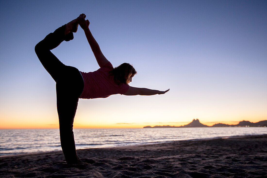 Frau in Yoga-Pose am Strand bei Sonnenaufgang