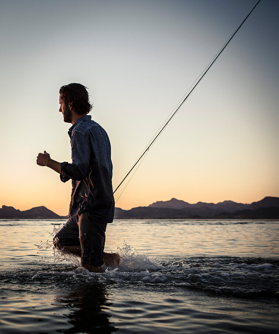 Man with Fly-fishing Pole Walking Through Shallow Water at Sunset