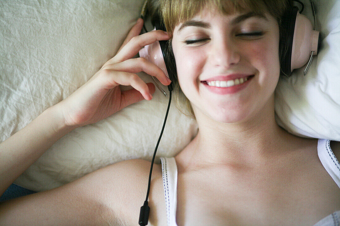 Junge lächelnde Frau, die sich mit Kopfhörern hinlegt