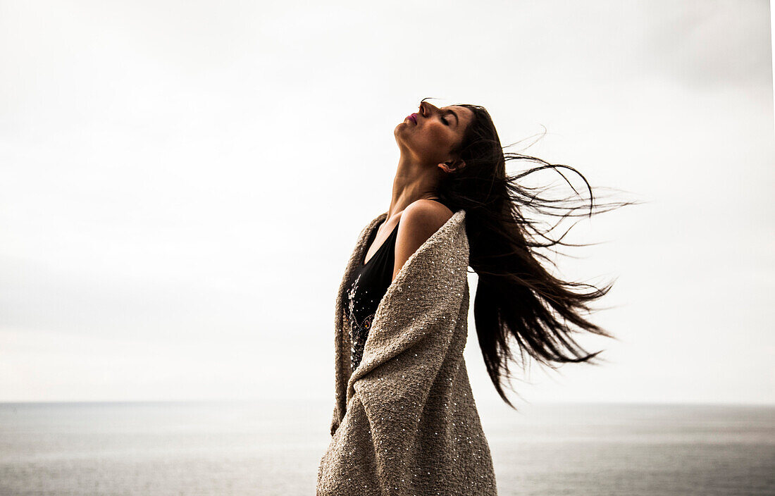 Young Woman Portrait with Head Back and Long Hair Blowing in Wind with Ocean in Background