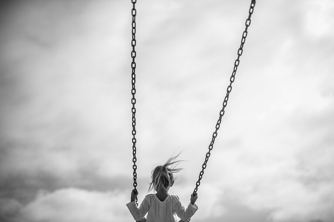 Girl on Swing Against Gray Sky, Rear View