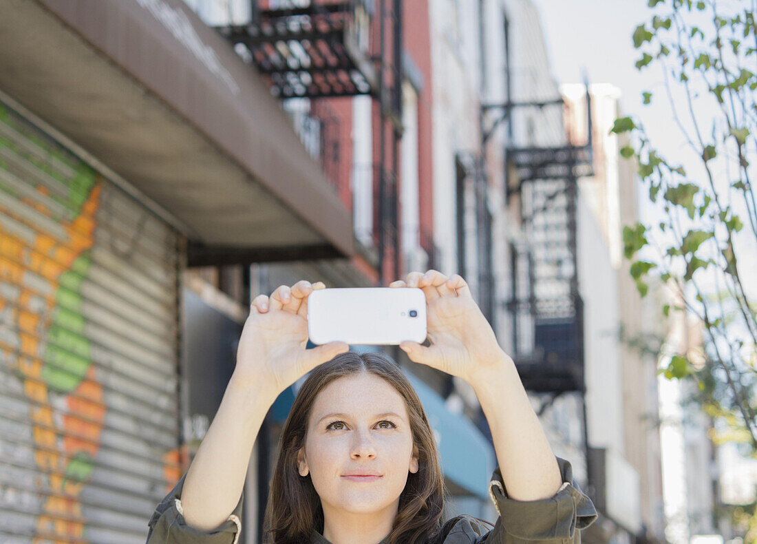 Caucasian woman taking cell phone photograph on urban sidewalk, C1