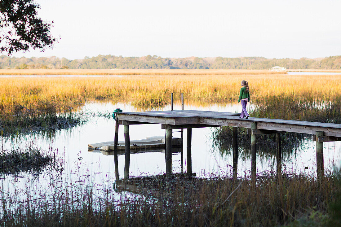 Caucasian girl walking on wooden dock in lake, C1