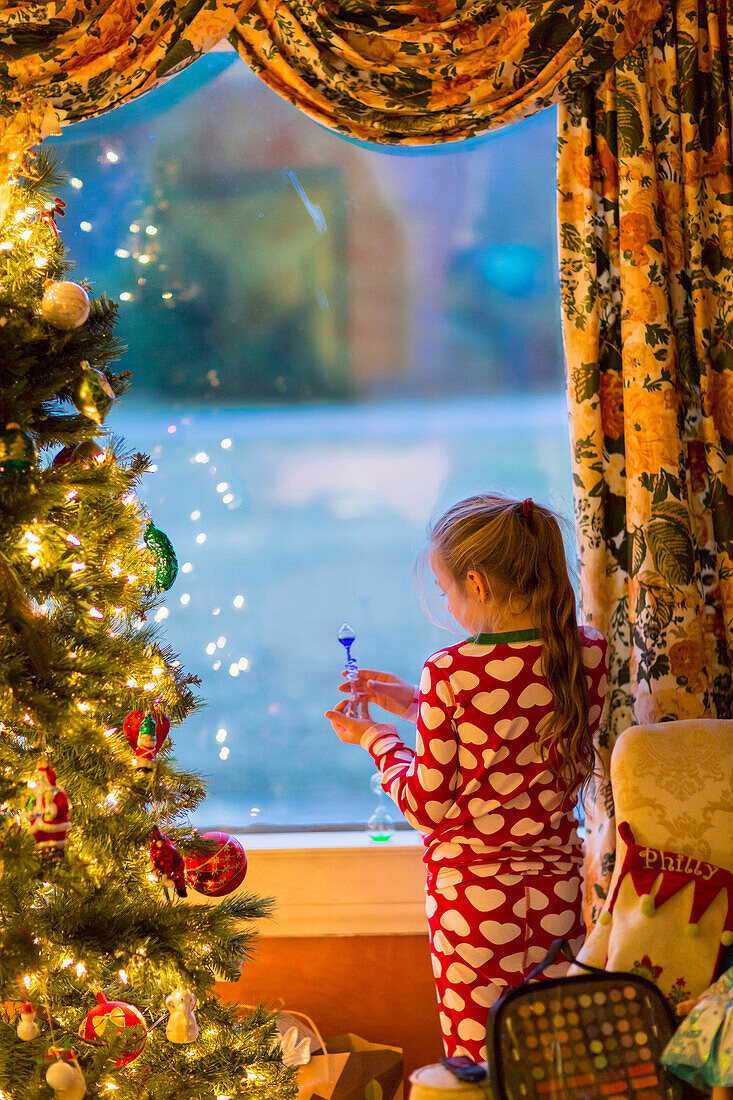 Caucasian girl opening present near Christmas tree, C1