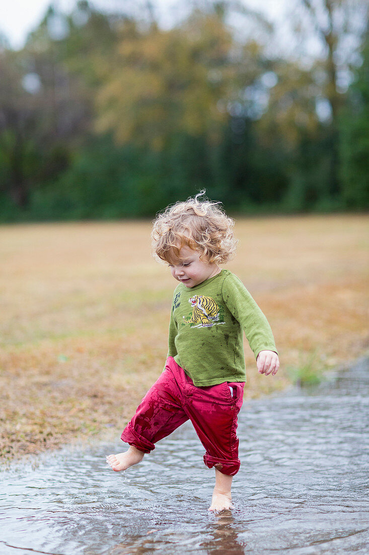 Caucasian baby boy splashing in puddle, C1