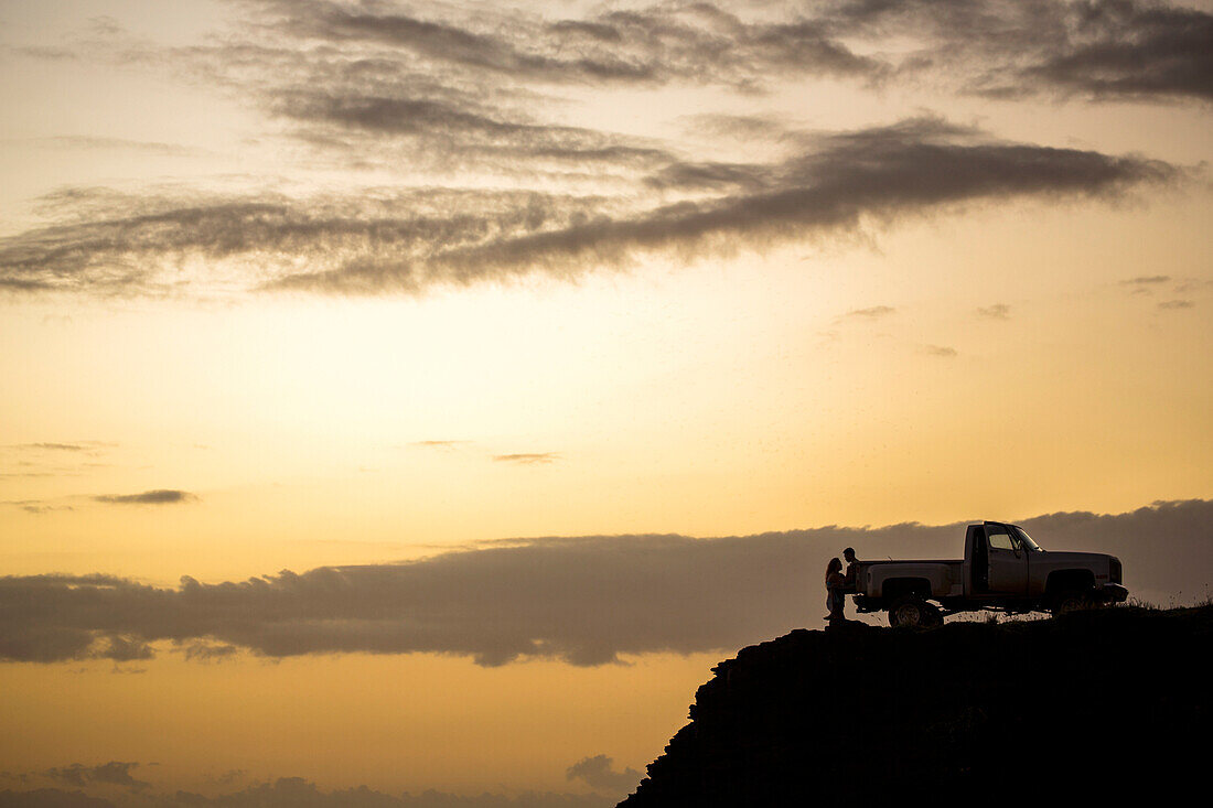 Silhouette of people sitting on pickup truck on cliff at sunset, C1