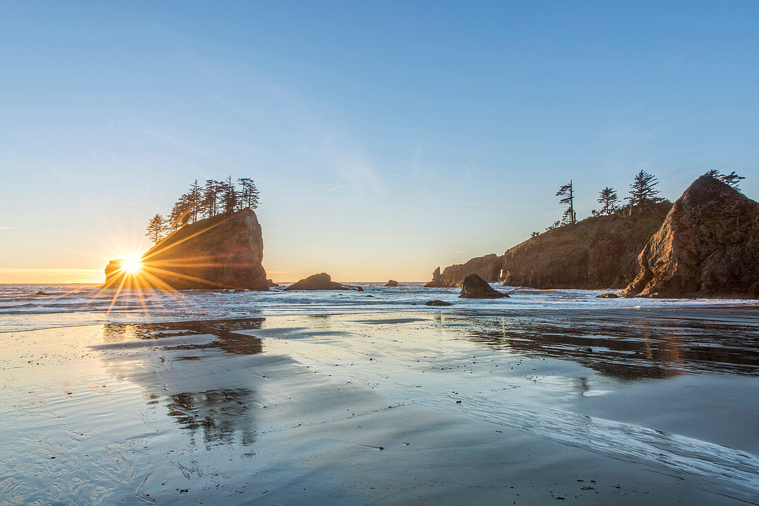 Sun rising over rock formations on beach, rural, Washington, USA