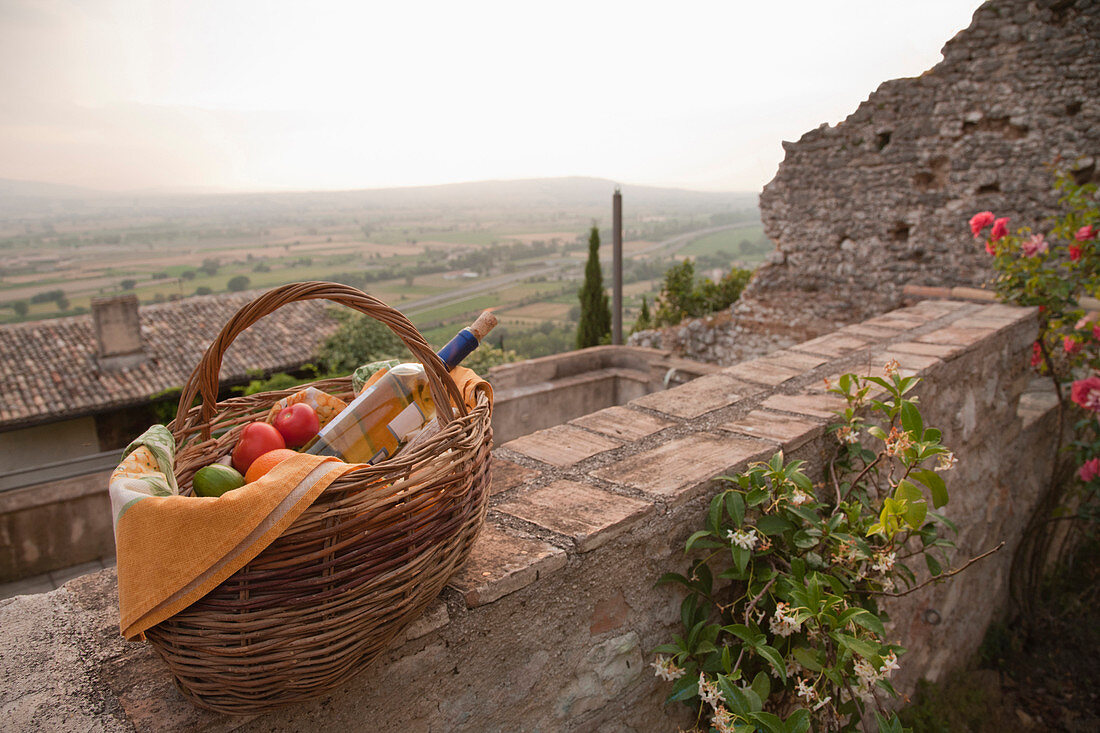 Basket of fresh fruit and wine on stone wall, Spoleto, Umbria, Italy