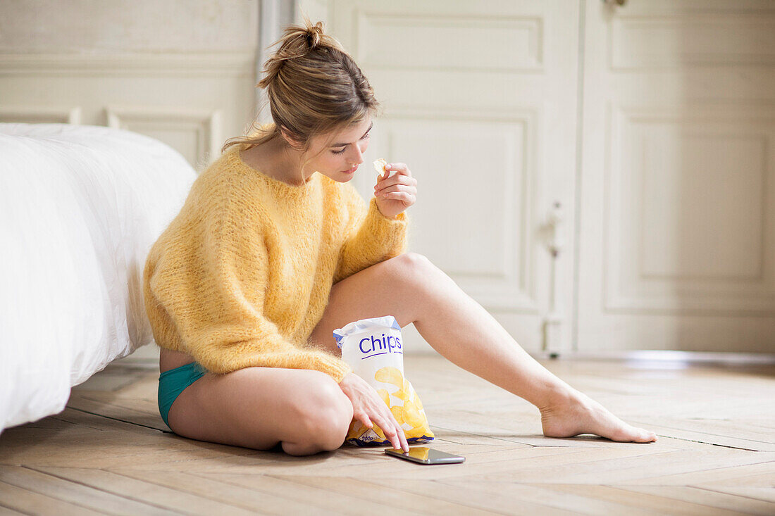 Woman using phone and eating chips
