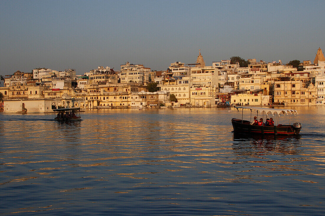 India, Rajasthan, city of Udaipur, a large view at sunset on the city and its ghats with two small boats on the lake Pichola